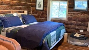 A cozy log cabin bedroom with a bed, a chair, and a pet bed. - Taylor`s Depot Cabin (Paonia)