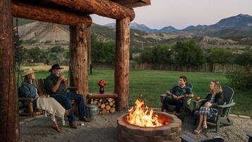 A rustic outdoor seating area with a fire pit, wooden furniture, and a view of a mountainous landscape.