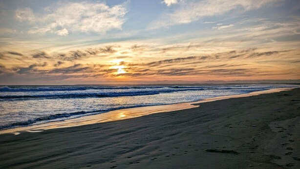 Une plage avec des vagues, un coucher de soleil et un ciel dégagé.