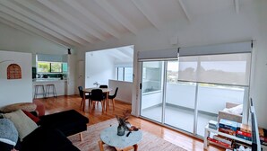 Un salon moderne avec un coin repas, de grandes portes-fenêtres coulissantes donnant sur un balcon et une cuisine à l’arrière-plan.