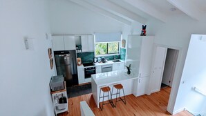 Une cuisine moderne avec des meubles blancs, un réfrigérateur en acier inoxydable, un four encastré et une fenêtre donnant sur un espace verdoyant.