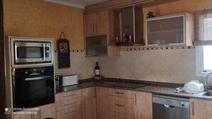 Una cocina con armarios de madera, microondas, lavavajillas, pileta y ventana con persianas.