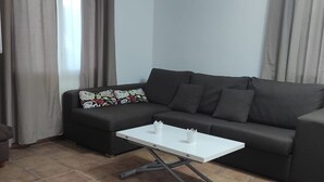 Un salón con un sofá gris oscuro, un pequeño reposapiés y una mesa de centro blanca.