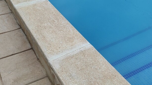 Una piscina con borde de baldosas, sillas de descanso y una pared de piedra.