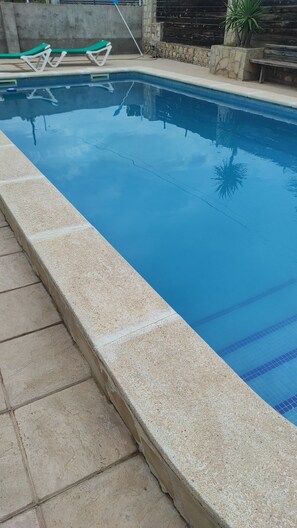Une piscine avec un bord carrelé, des chaises longues et un mur en pierre.