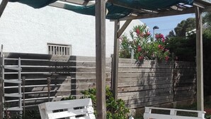 Un patio al aire libre con una pérgola de madera, bancos blancos de madera y piso de baldosas.