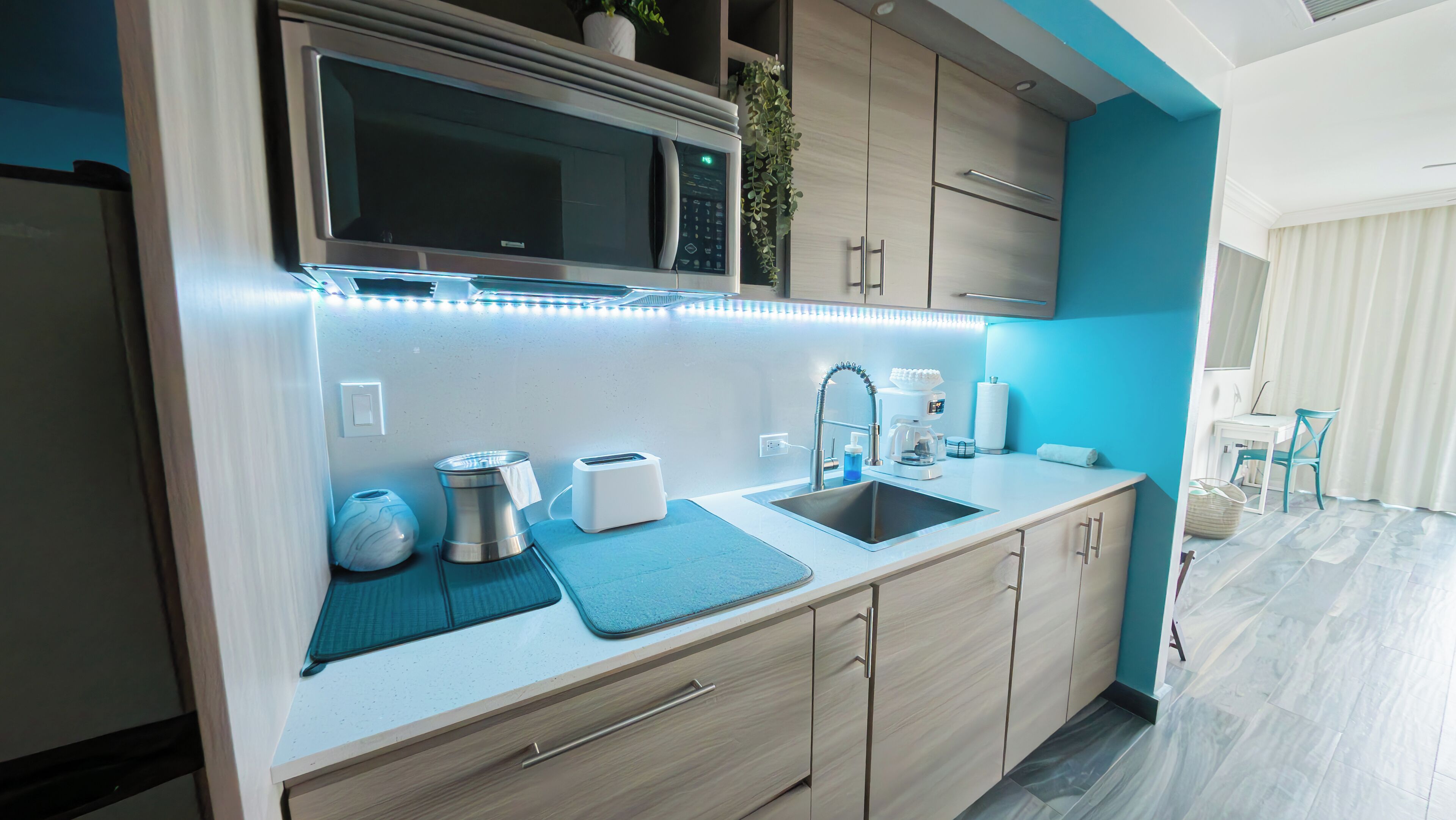 A modern kitchen with a microwave, toaster, sink, and a small dining area with a chair.