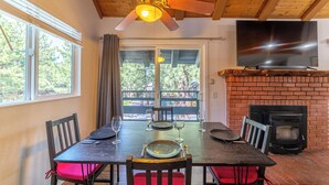 A dining area with a table set for four, a ceiling fan, a fireplace, and a TV mounted on the wall. - Remodeled Mid-Town Beauty with Spa Retreat 547 (Mammoth Lakes)