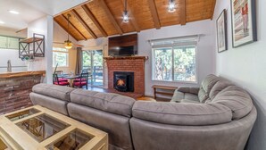 A modern living room with a brick fireplace, wooden ceiling beams, and a large sectional sofa. - Remodeled Mid-Town Beauty with Spa Retreat 547 (Mammoth Lakes)