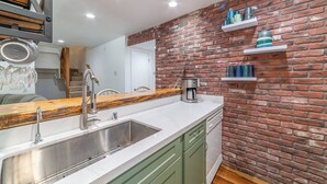 A kitchen with a brick wall, green cabinets, a stainless steel sink, and white countertops. - Remodeled Mid-Town Beauty with Spa Retreat 547 (Mammoth Lakes)