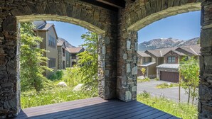 A covered outdoor area with stone arches, a wooden deck, and a view of residential buildings and mountains in the background.