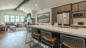A modern kitchen with a large island, bar stools, and a view of the living area.
