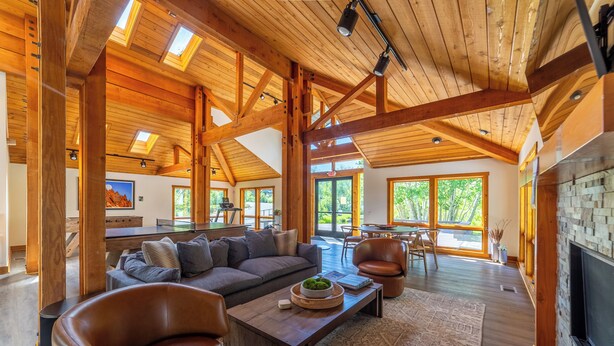 A spacious living area with a wooden ceiling, large windows, a fireplace, and leather furniture.