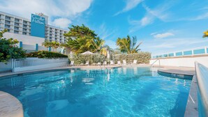 A hotel pool area with clear blue water, lounge chairs, and palm trees. - Mesmerizing Ocean View King Bed Near Beaches (San Juan)