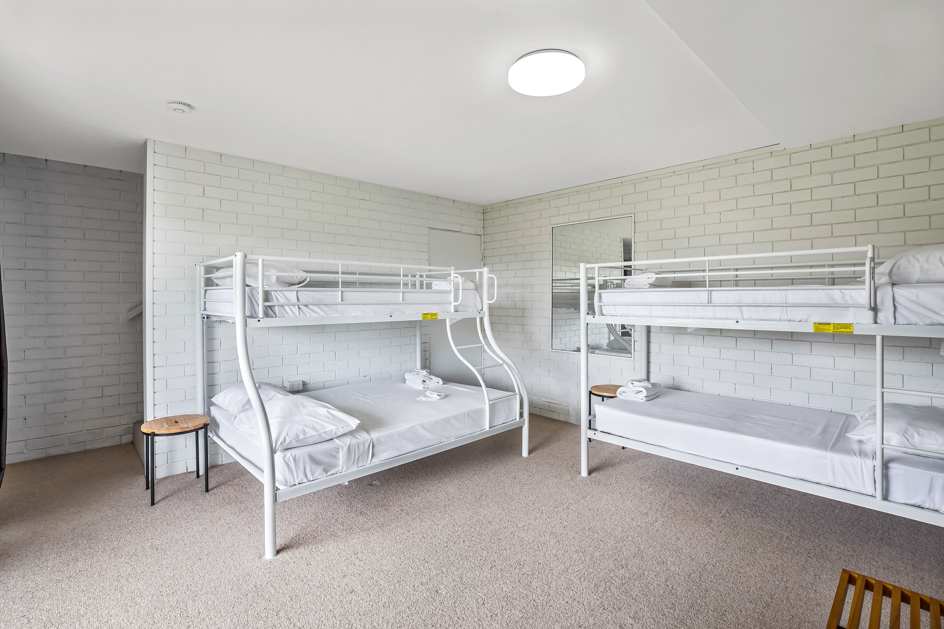 A room with two bunk beds, a small wooden stool, and a mirror on the wall.