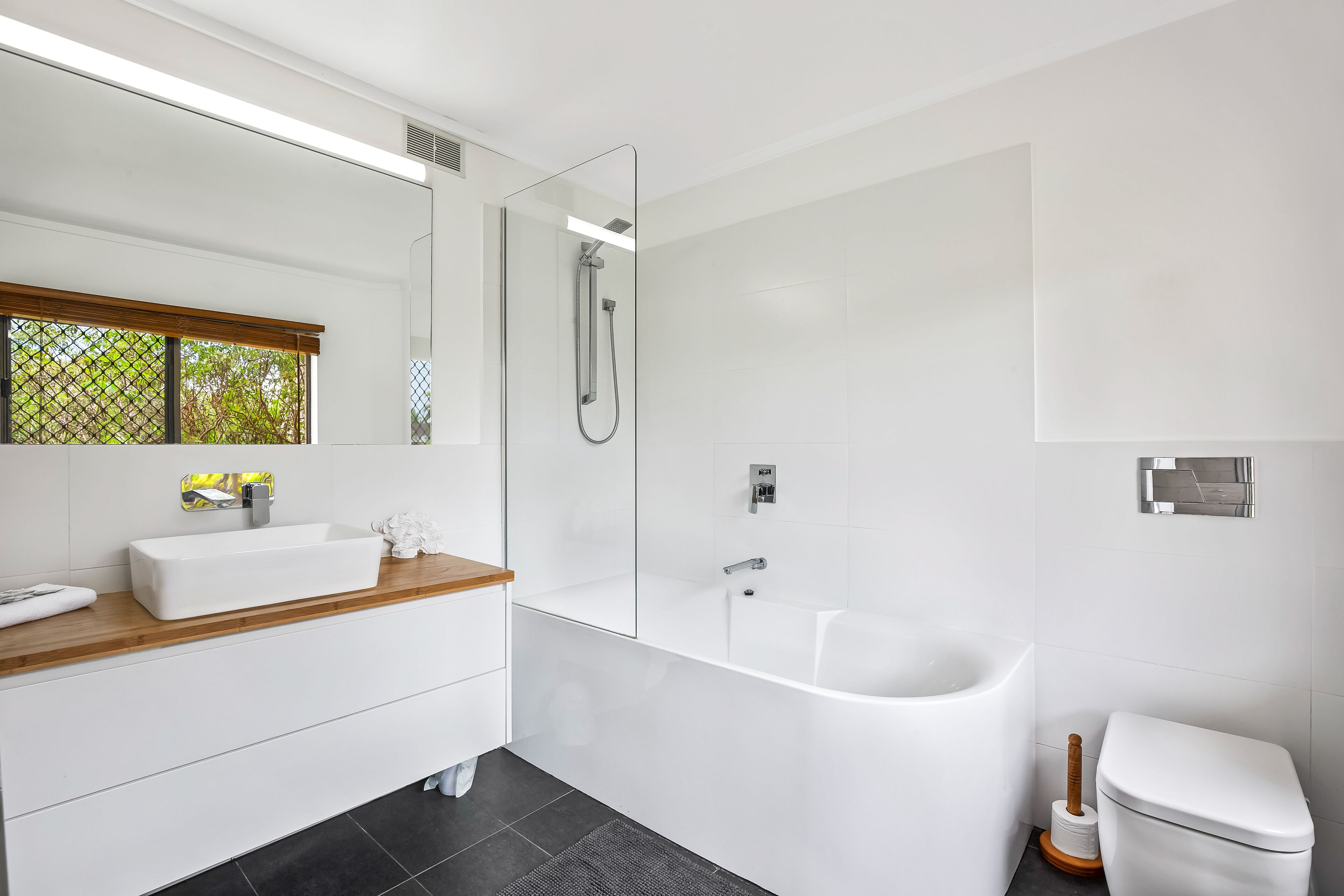 Un bagno moderno con uno specchio grande, un lavandino bianco, una vasca e un water.