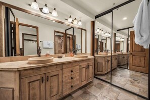 A modern bathroom with a large mirror, two sinks, wooden cabinets, and a tiled floor. - 1BR Ski in Ski Out Steps to Lifts (Park City)