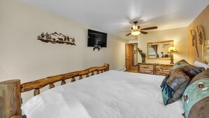 A bedroom with a wooden bed, a ceiling fan, a mounted TV, and a mirror above a dresser. - 1BR Ski in Ski Out Steps to Lifts (Park City)