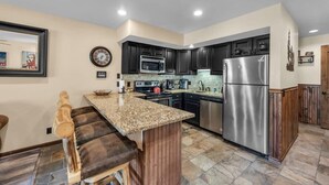 A modern kitchen with granite countertops, stainless steel appliances, and dark cabinetry. - 1BR Ski in Ski Out Steps to Lifts (Park City)