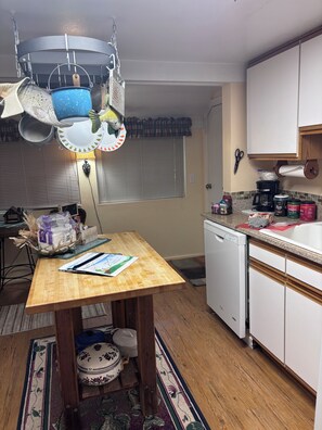 A kitchen with a wooden table, a hanging pot rack, and a white dishwasher.