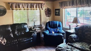 A living room with a ceiling fan, a black leather sofa, a blue armchair, and a patterned armchair. - 2 bedroom cabin in mineral (Mineral)