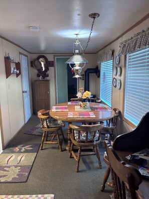 A dining area with a wooden table, chairs, a ceiling fan, and a wall-mounted clock. -  2 Bedroom rustic cabin in Mineral minutes to entrance of Lassen Park. (Mineral)