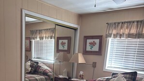 A bedroom with a bed, a ceiling fan, a window with blinds, a bedside table with a lamp, and a mirror. - 2 bedroom cabin in mineral (Mineral)