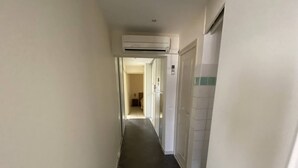 Un pasillo estrecho con piso de baldosas, paredes blancas y un equipo de aire acondicionado instalado en el techo.