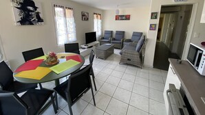 Un comedor con una mesa redonda, sillas y un televisor. Hay sofás de mimbre y un reloj en la pared.