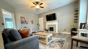 Una sala de estar con un sofá gris, una mesa de centro de madera, una chimenea y un televisor montado encima.