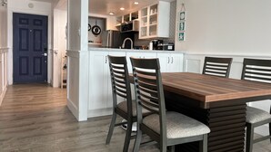 A modern kitchen with white cabinets, a central island, and a dining area with wooden chairs. - Beachfront condo with stunning ocean views. Pet-Friendly! (Galveston)