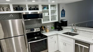 A modern kitchen with stainless steel appliances, white cabinetry, and a marble countertop. - Beachfront condo with stunning ocean views. Pet-Friendly! (Galveston)