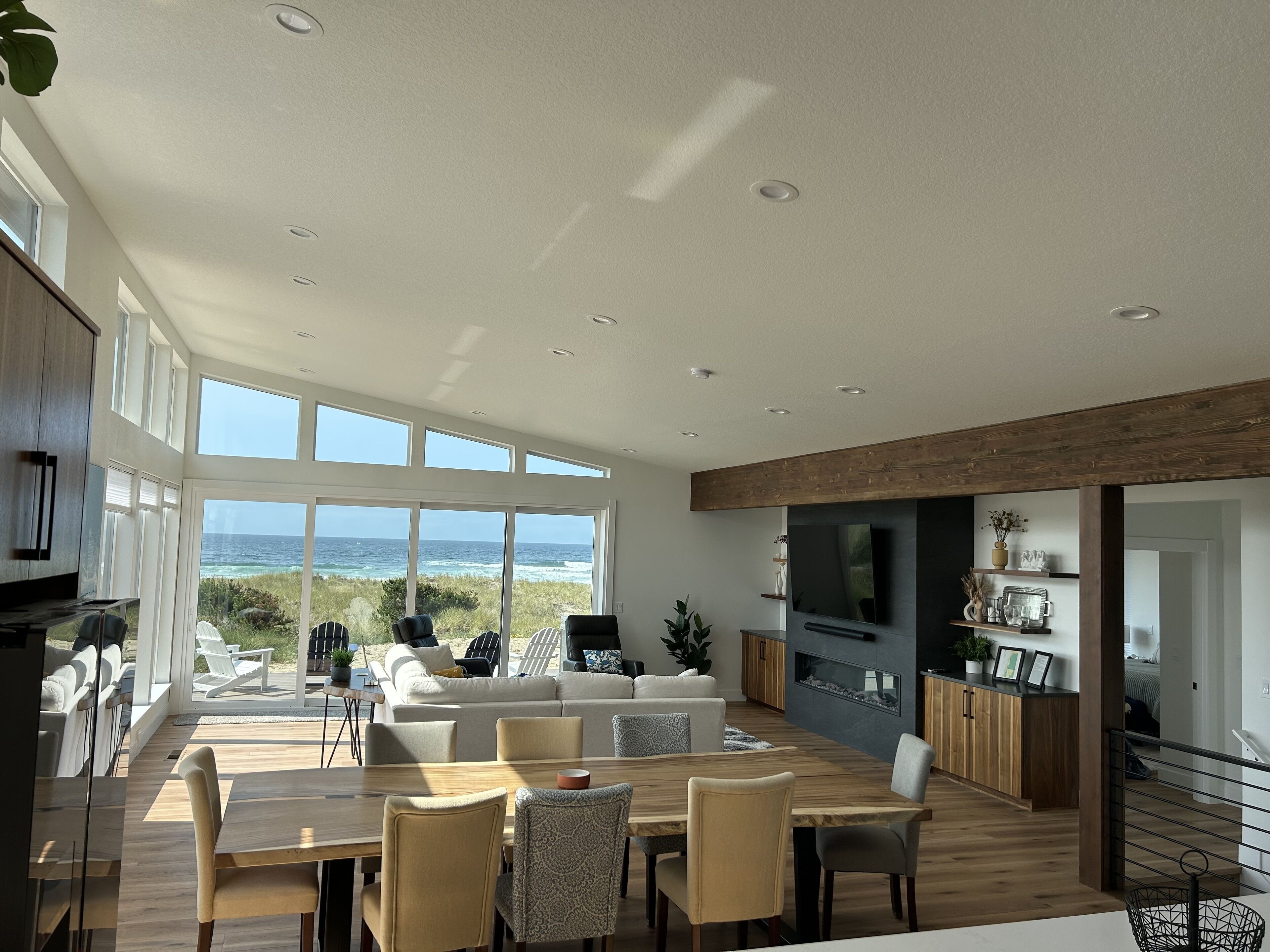 Un vaste espace de vie comprenant une grande table à manger en bois, des sièges confortables et une vue sur l’océan.