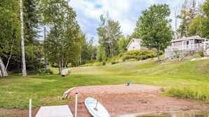Ejendom ved søen med en badebro, et paddleboard og et hus i baggrunden.