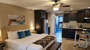 Une chambre à coucher comprenant un lit, un banc, une table de chevet, un ventilateur de plafond et un tableau accroché au mur.