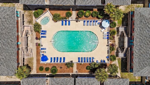 An aerial view of a resort with a central swimming pool, sun loungers, and palm trees.