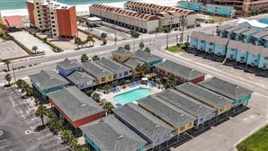 A beachfront hotel with multiple-story buildings, a swimming pool, and a parking lot.
