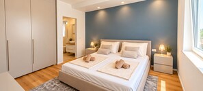 A modern bedroom with a large bed, bedside tables, a wardrobe, and a view of the outside.