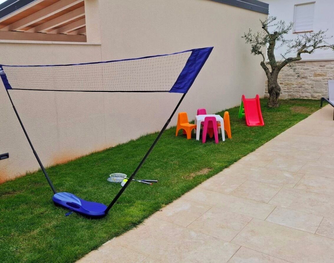 A backyard with a badminton net, colorful plastic chairs, a small table, and a slide.