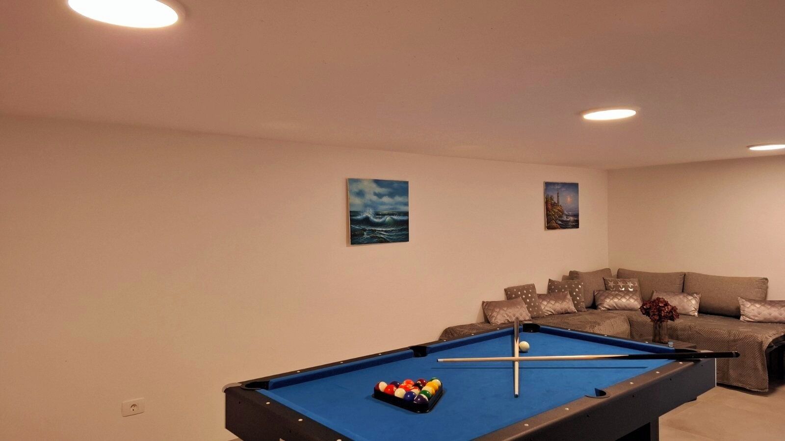 Ein Billardtisch mit Kugeln, eine Couch und zwei Bilder an der Wand.