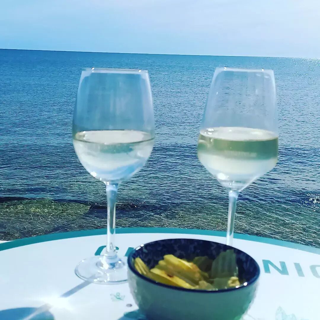 Deux verres à vin et un bol de nourriture sont posés sur une table, près de la mer.