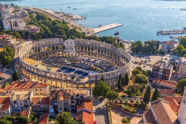 An ancient Roman amphitheater surrounded by urban buildings and a marina.