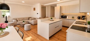 A modern kitchen with a central island, a dining area with a round table, and a living room with a sofa and ottoman.