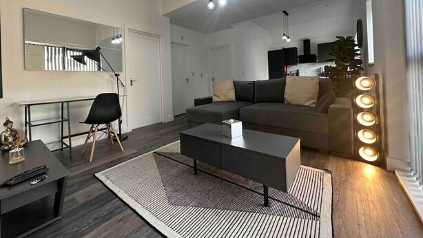 A modern living room with a sofa, coffee table, and a desk with a chair. There is a large mirror on the wall and a plant in the corner.