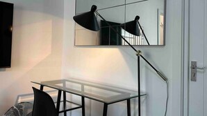 A modern room with a glass table, a black desk lamp, and a large mirror on the wall.