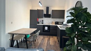 A modern kitchen with dark cabinetry, a wooden dining table, and a large plant.