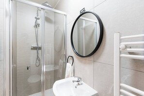 A modern bathroom with a glass-enclosed shower, a white sink, and a round mirror on the wall. - NH - F1 · Comfortable Modern 1 bed Apt (Cardiff)