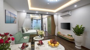 Een moderne woonkamer met een bank, een eettafel met een fles en glazen, een fruitschaal en een televisie aan de muur.