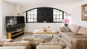 Una sala de estar moderna con un televisor de pantalla plana grande, una mesa de centro de madera y un sofá color beige.