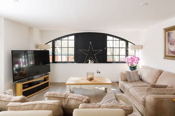 A modern living room with a large flat-screen TV, a wooden coffee table, and a beige sofa.